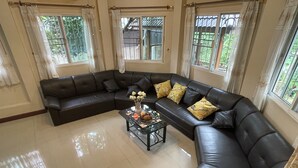Un salon comprenant un canapé d’angle en cuir noir, une table basse en verre agrémentée d’objets décoratifs et de grandes fenêtres avec des rideaux.