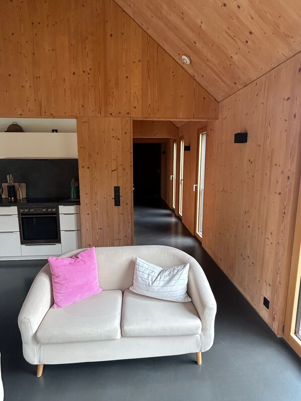 Ein modernes Interieur mit einer Couch, Holzwänden, einer Küchenzeile und einem Flur.
