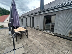 A patio with a table and chairs, a covered umbrella, and a building with large windows and a metal roof.