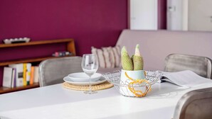 Ein Esstisch mit weißer Tischdecke, einem Weinglas aus Glas, einem Metallkorb mit einem Kaktus und einem Buch.