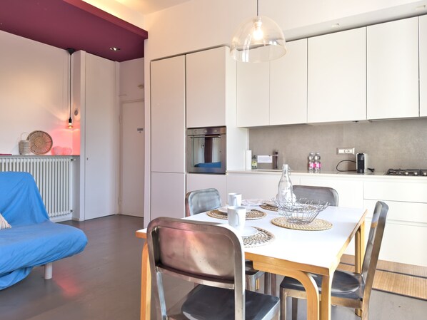 A modern kitchen with white cabinets, a dining table with chairs, and a blue sofa in a living area.