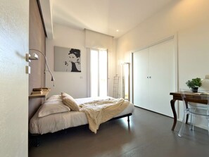 A bedroom with a bed, bedside table, lamp, and a painting on the wall.