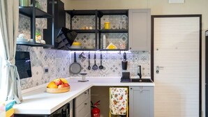 A compact kitchen with white cabinets, a countertop with a fruit bowl, hanging utensils, and a fire extinguisher. - Il rifugio Felice, charming apartment with private parking (Gallinaro)