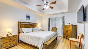 A bedroom with a wooden bed, a nightstand, a bench, a chair, a ceiling fan, and a TV mounted on the wall.