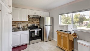 A modern kitchen with white cabinets, stainless steel appliances, and a view of the outdoors through a large window. - Quaint Home 16 Mi to Bear Lake: Fish, Hike & Golf! (Montpelier)