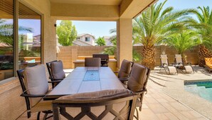 An outdoor patio with a dining table and chairs, a pool, and palm trees.