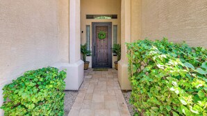 A narrow pathway leading to a door with a wreath, flanked by potted plants and a textured wall.