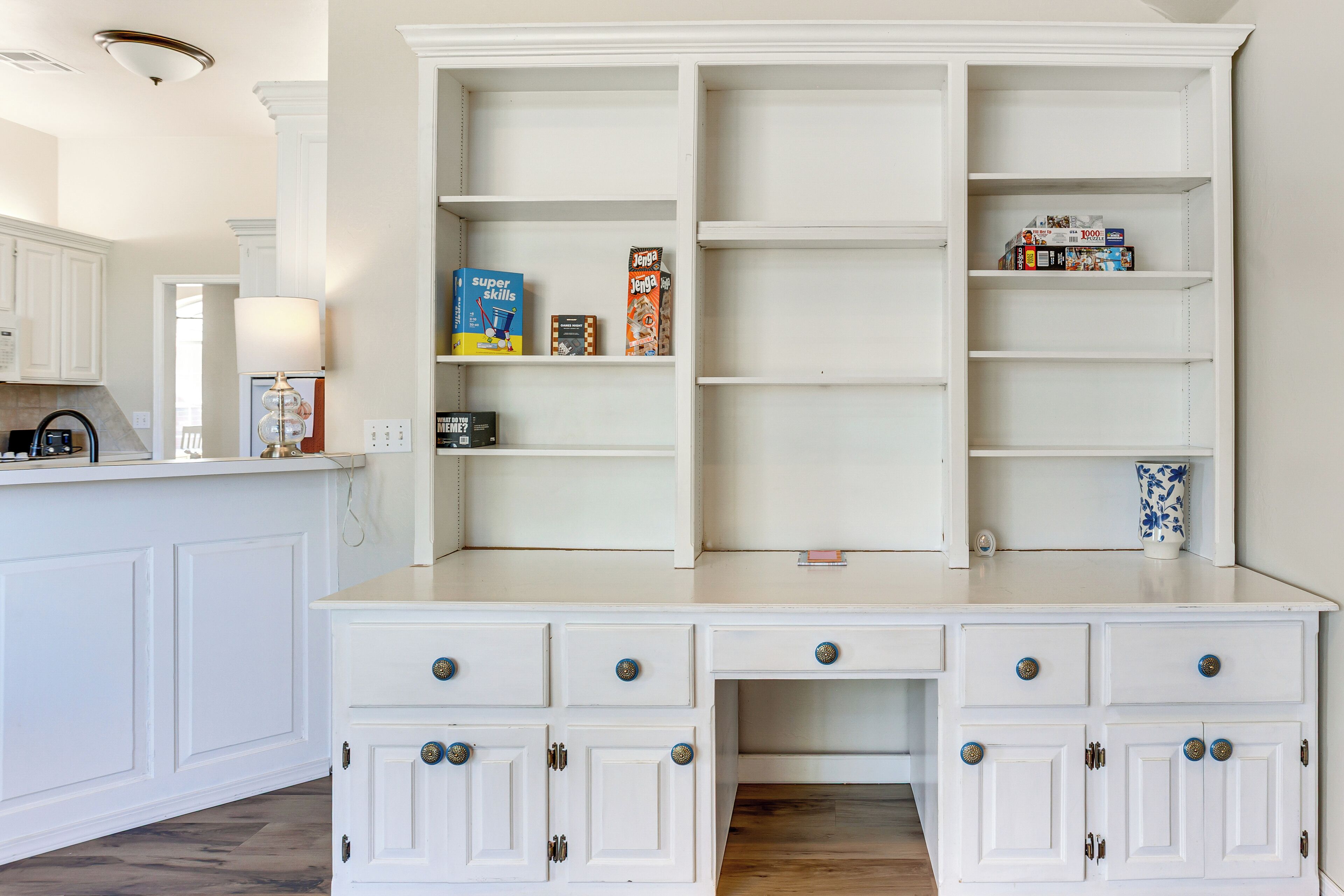 A kitchen with white cabinetry, a countertop, and a built-in bookshelf.