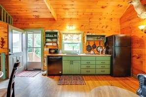 A wooden cabin kitchen with a refrigerator, green cabinets, and a window with curtains. - On 30 Acres w/ Trails & Garden: Stockholm Cabin! (Stockholm)