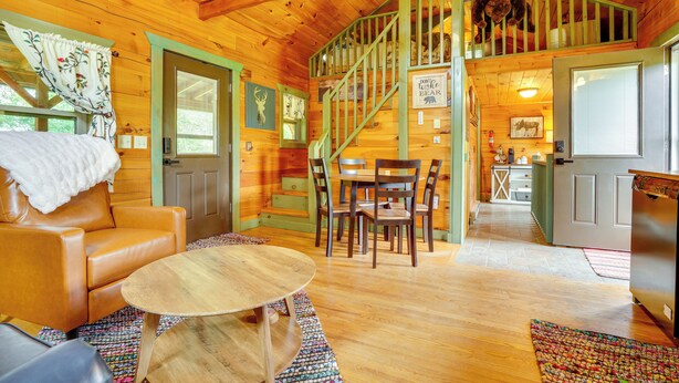 A cozy cabin interior with a wooden staircase, a dining area, and a living room with a leather couch and a round table.