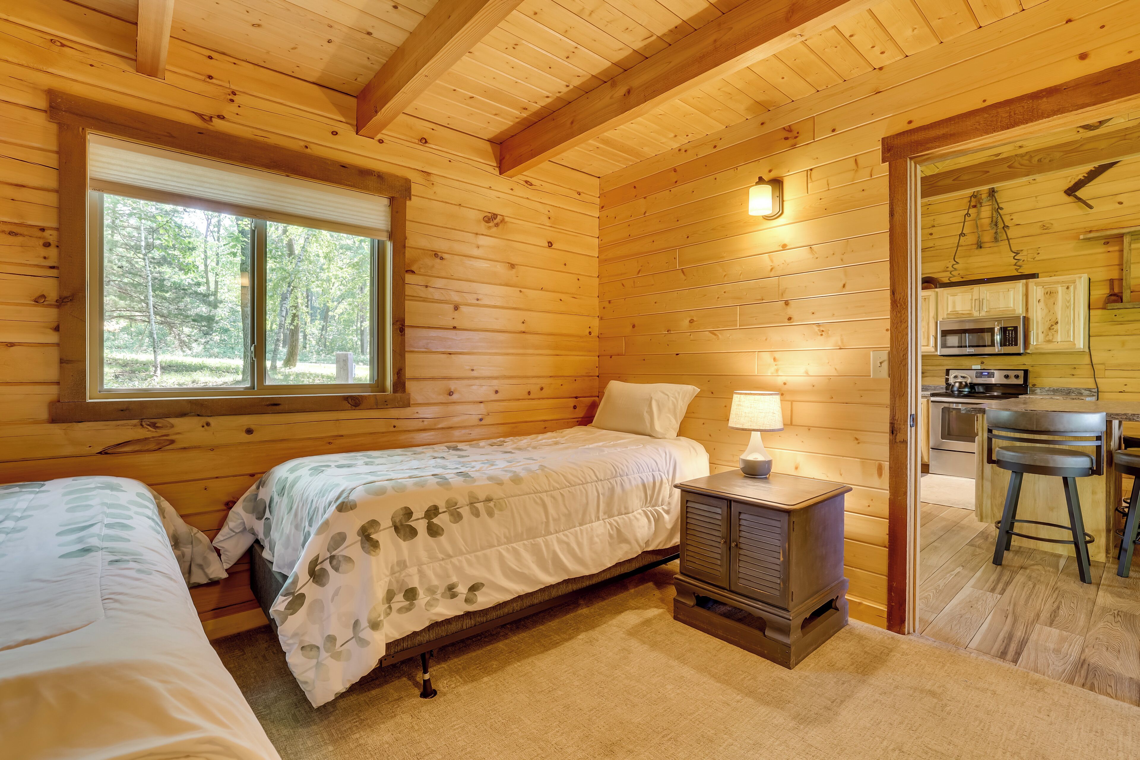 Une cabane en bois avec deux lits, une petite kitchenette et une fenêtre donnant sur la forêt.