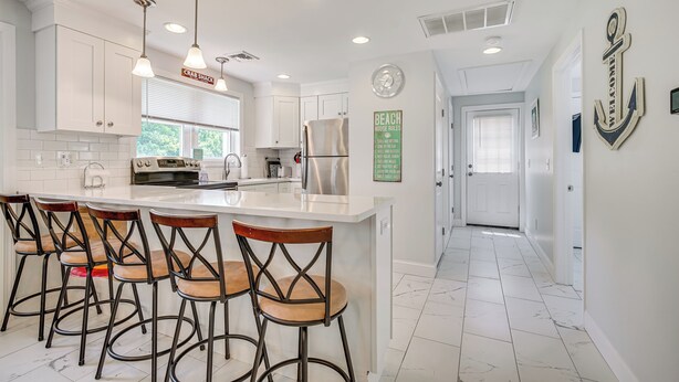 A modern kitchen with white cabinets, a large island with bar stools, stainless steel appliances, and a 'Welcome' anchor decoration on the wall. - Family Retreat in Old Lyme Gated Miami Beach (Old Lyme)