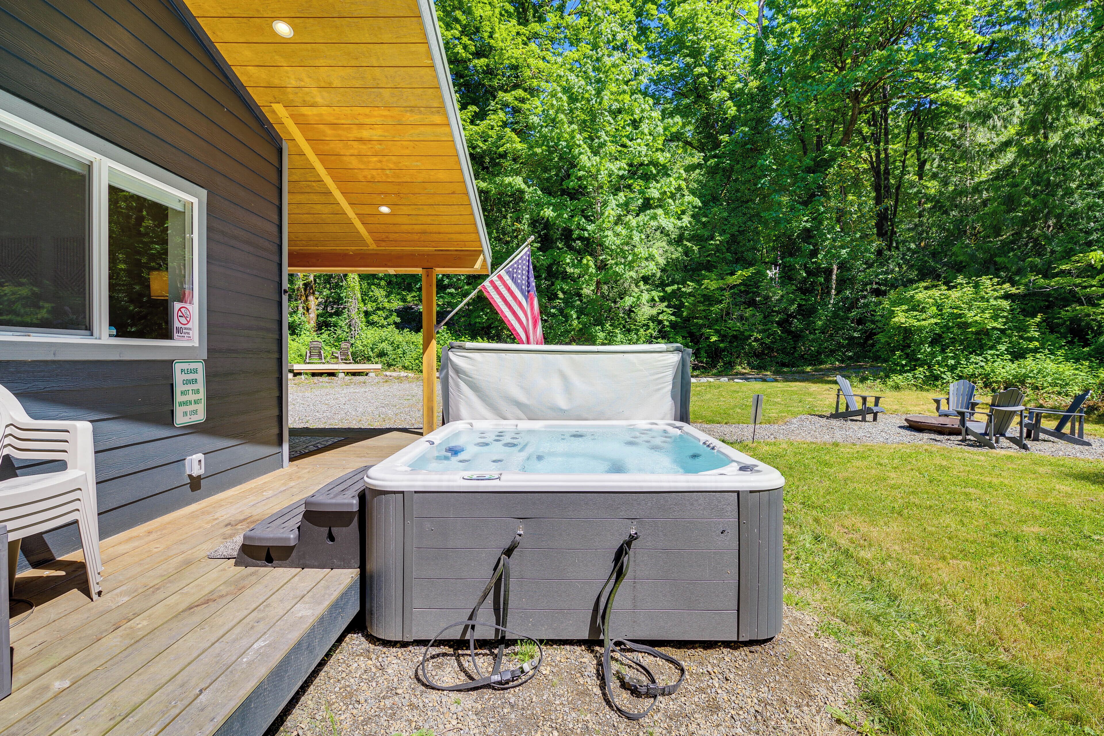 Ein Whirlpool auf einer Holzterrasse mit einer amerikanischen Flagge, umgeben von einem grünen Rasen und Bäumen.