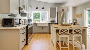A modern kitchen with white cabinets, stainless steel appliances, and a wooden dining table.