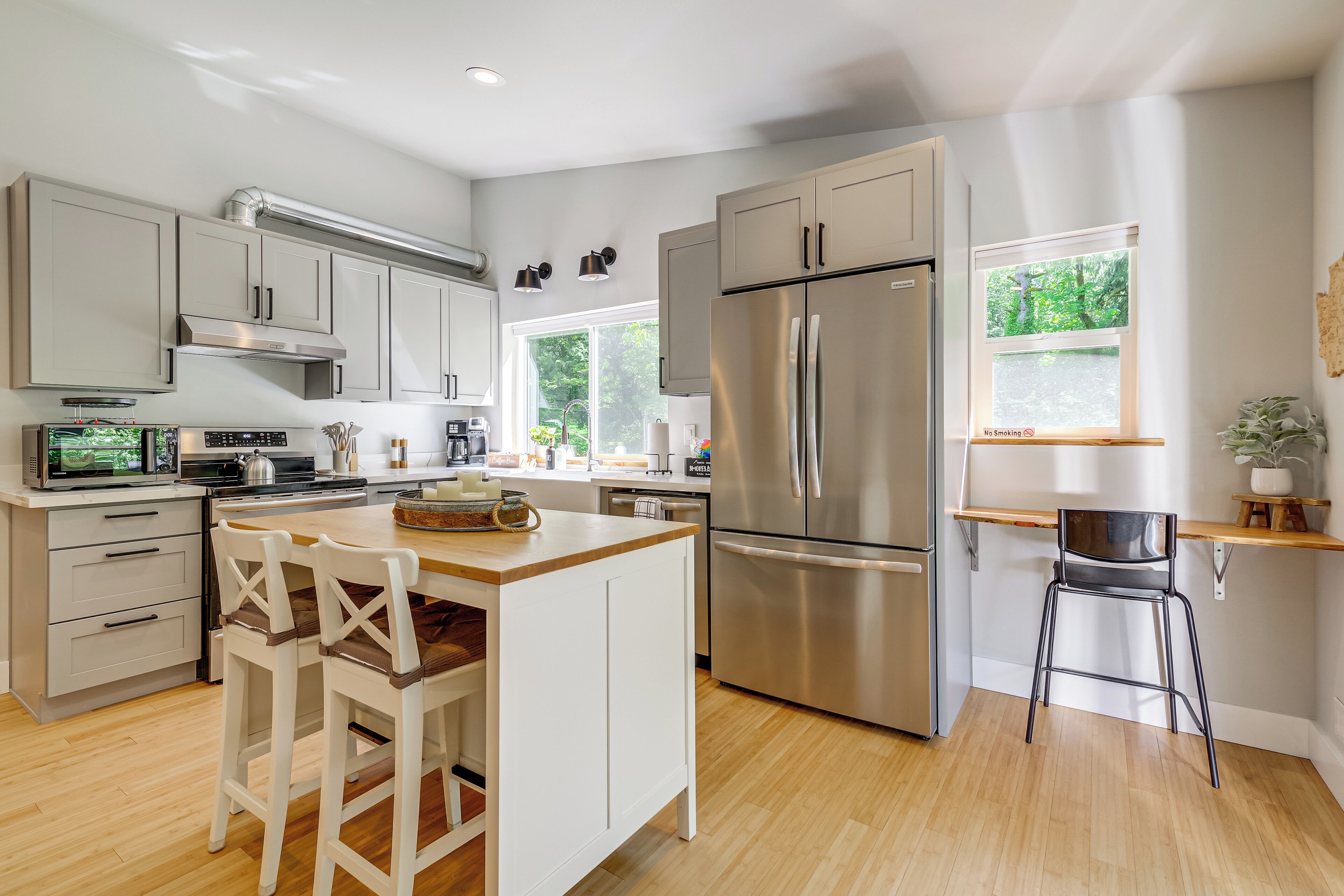 A modern kitchen with stainless steel appliances, wooden flooring, and a central island with bar stools.