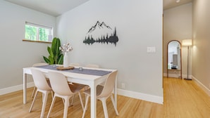 A dining area with a white table, four chairs, a potted plant, and a wall decal of a mountain range.