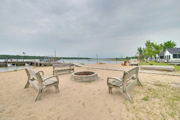 A sandy beach area with a fire pit and benches, overlooking a body of water with docks and boats. - Lake Huron Shoreline Gem: Free Boats, Sandy Beach! (Cedarville)