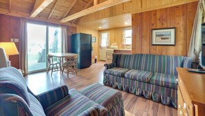 Un acogedor interior de cabaña con techo de madera, un sofá a rayas, una mesa de comedor y una zona de cocina.