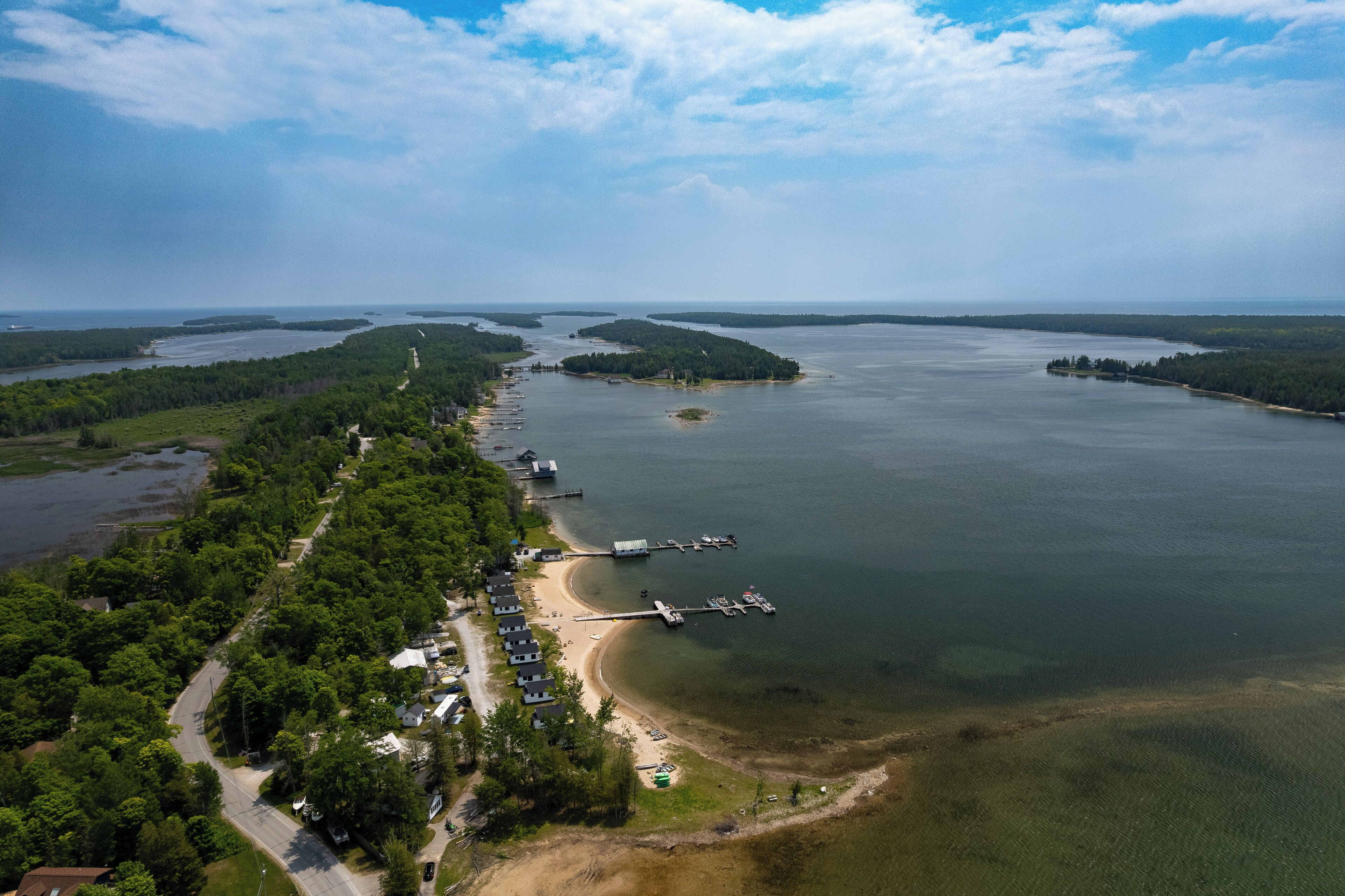 An aerial view of a coastal area with a dock, a beach, and a row of houses along the shore.