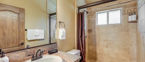 Une salle de bain avec un lavabo sur un plan de travail en granit, un meuble en bois, des toilettes et un espace douche avec une fenêtre.