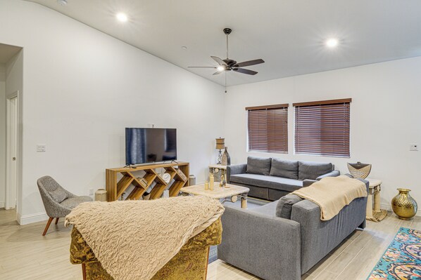 A modern living room with a grey sofa, a small table, a TV, and a ceiling fan.