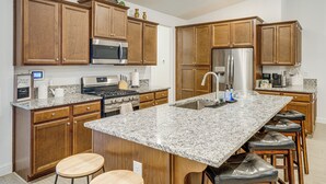 A modern kitchen with granite countertops, stainless steel appliances, wooden cabinets, and a central island with stools. - 9 Mi to Dtwn Bakersfield: Pet-friendly Home (Bakersfield)