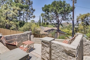 An outdoor patio area with stone walls, wooden furniture, and a view of surrounding trees and hills. - The Storybook Cottage: Every Stay Tells a Story! (Thousand Oaks)