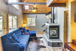 A cozy living room with a blue sofa, a fireplace, and a ceiling fan. - The Storybook Cottage: Every Stay Tells a Story! (Thousand Oaks)