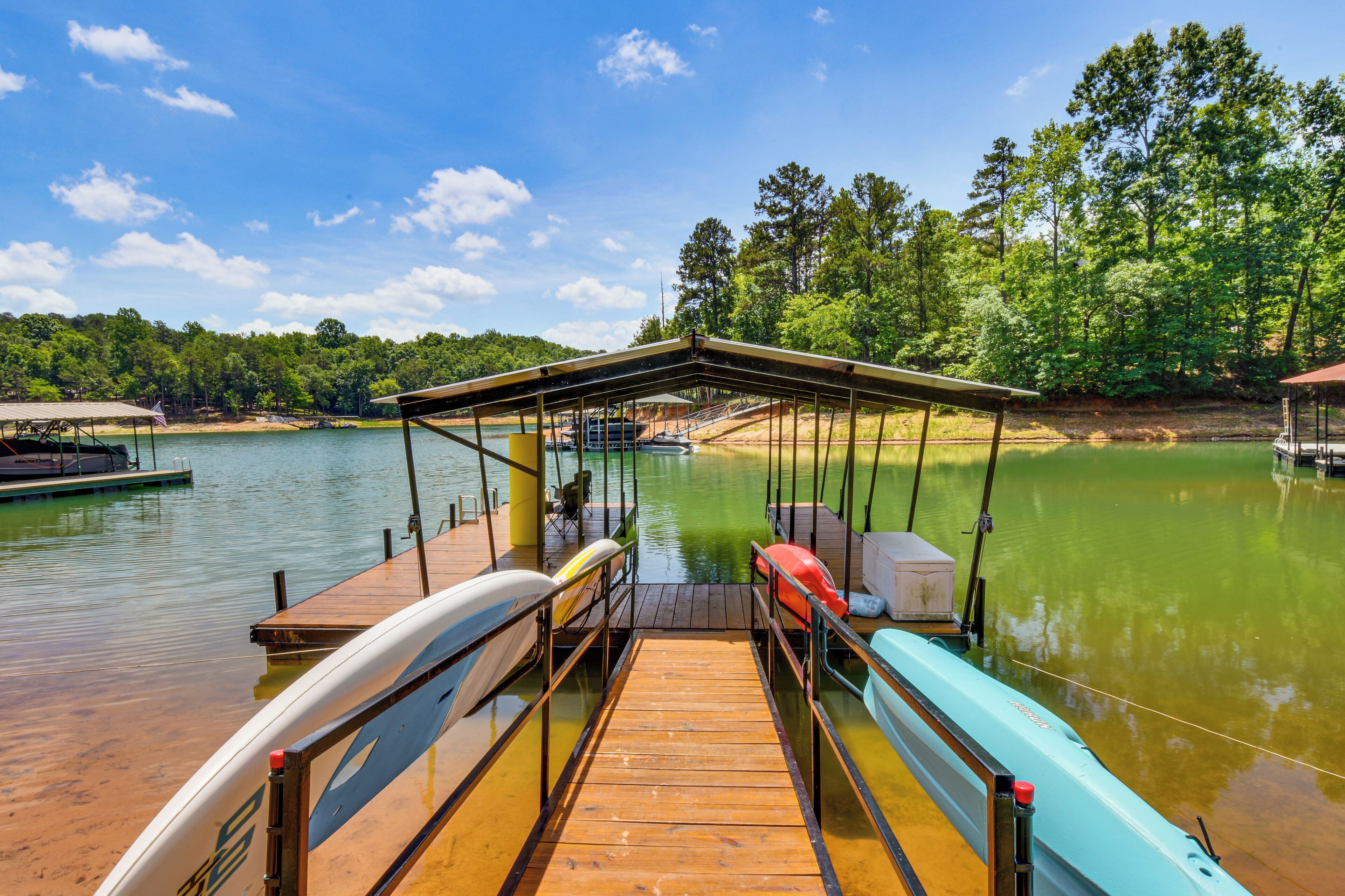 A wooden dock extending into a calm lake with boats docked, surrounded by trees and a clear sky.