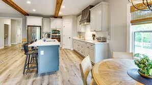 A modern kitchen with a central island, wooden beams, and a dining area with a round table and chairs.
