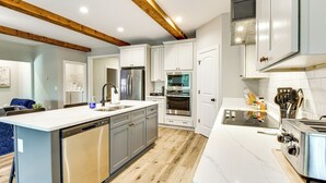 A modern kitchen with white cabinets, stainless steel appliances, and wooden beams on the ceiling.