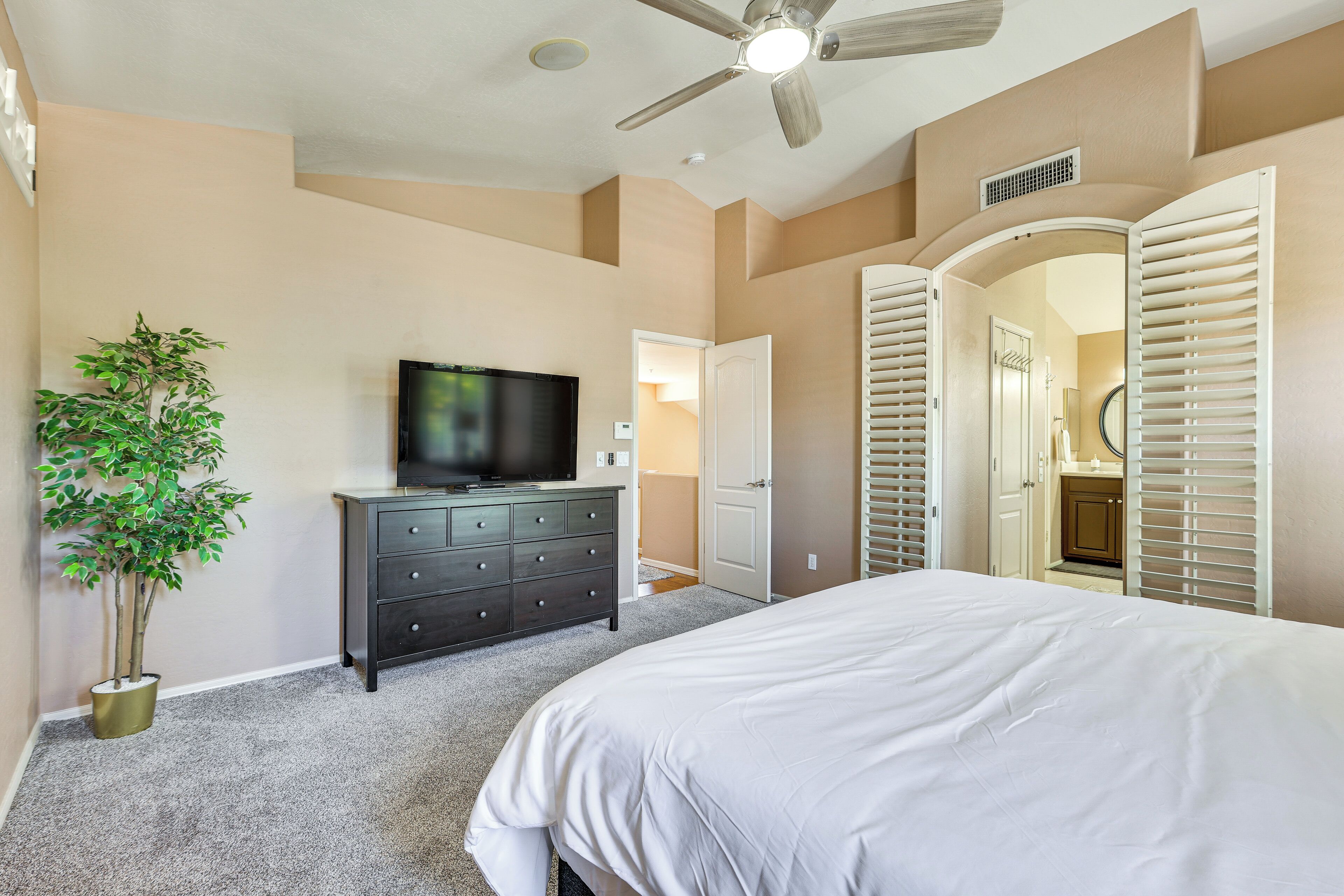 A bedroom with a bed, a dresser, a television, and a ceiling fan.