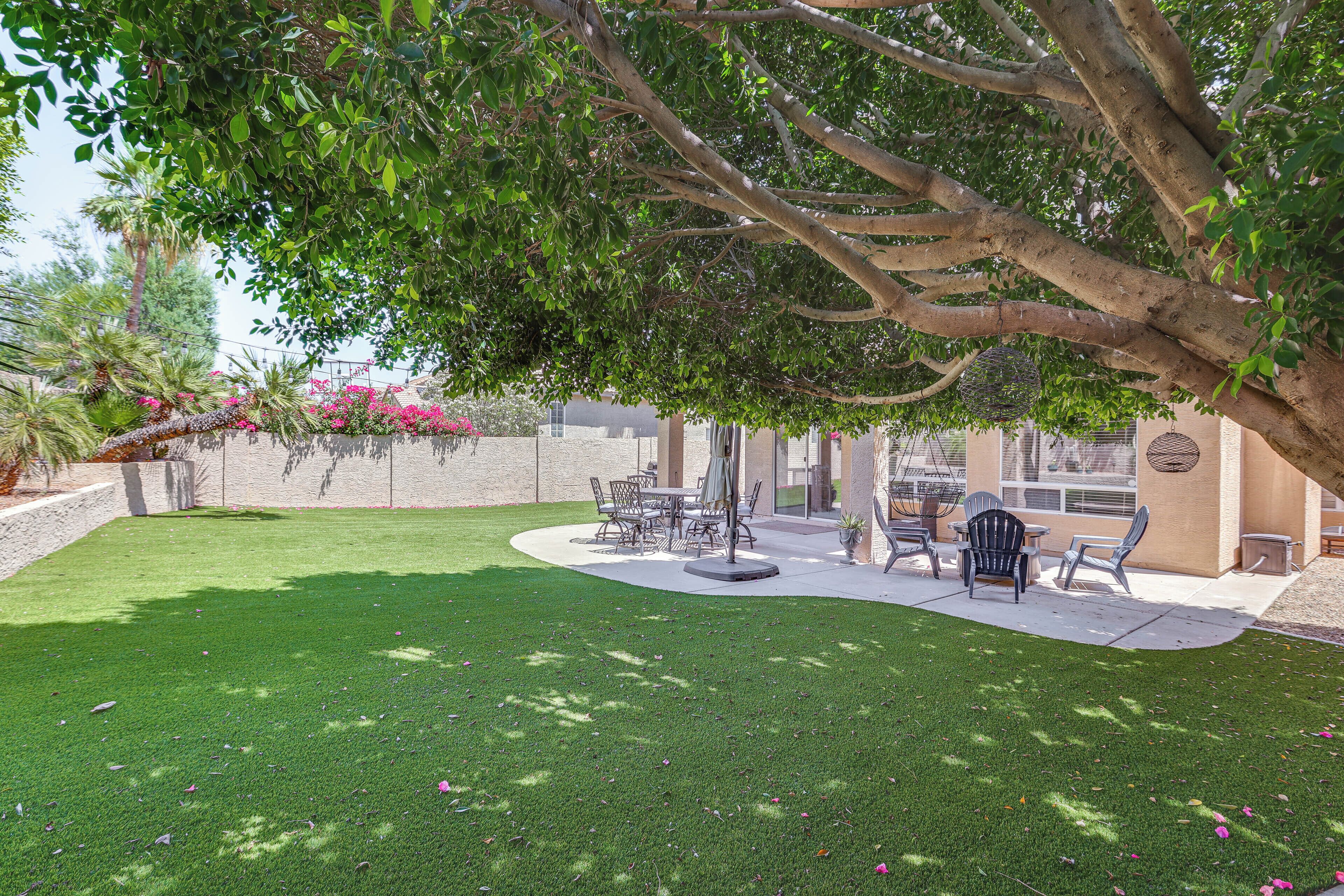 A patio area with a dining table and chairs, surrounded by a well-maintained lawn and a large tree providing shade.