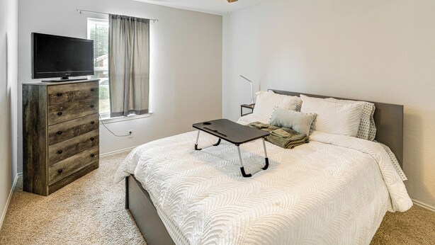Een slaapkamer met een bed, een kaptafel, een televisie en een plafondventilator.
