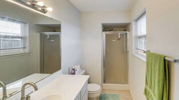 A bathroom with a white sink, mirror, and toilet, a shower with a glass door, and a green towel hanging on the wall.