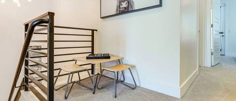 A staircase with a metal railing, a small table with a chair, and a framed picture on the wall.