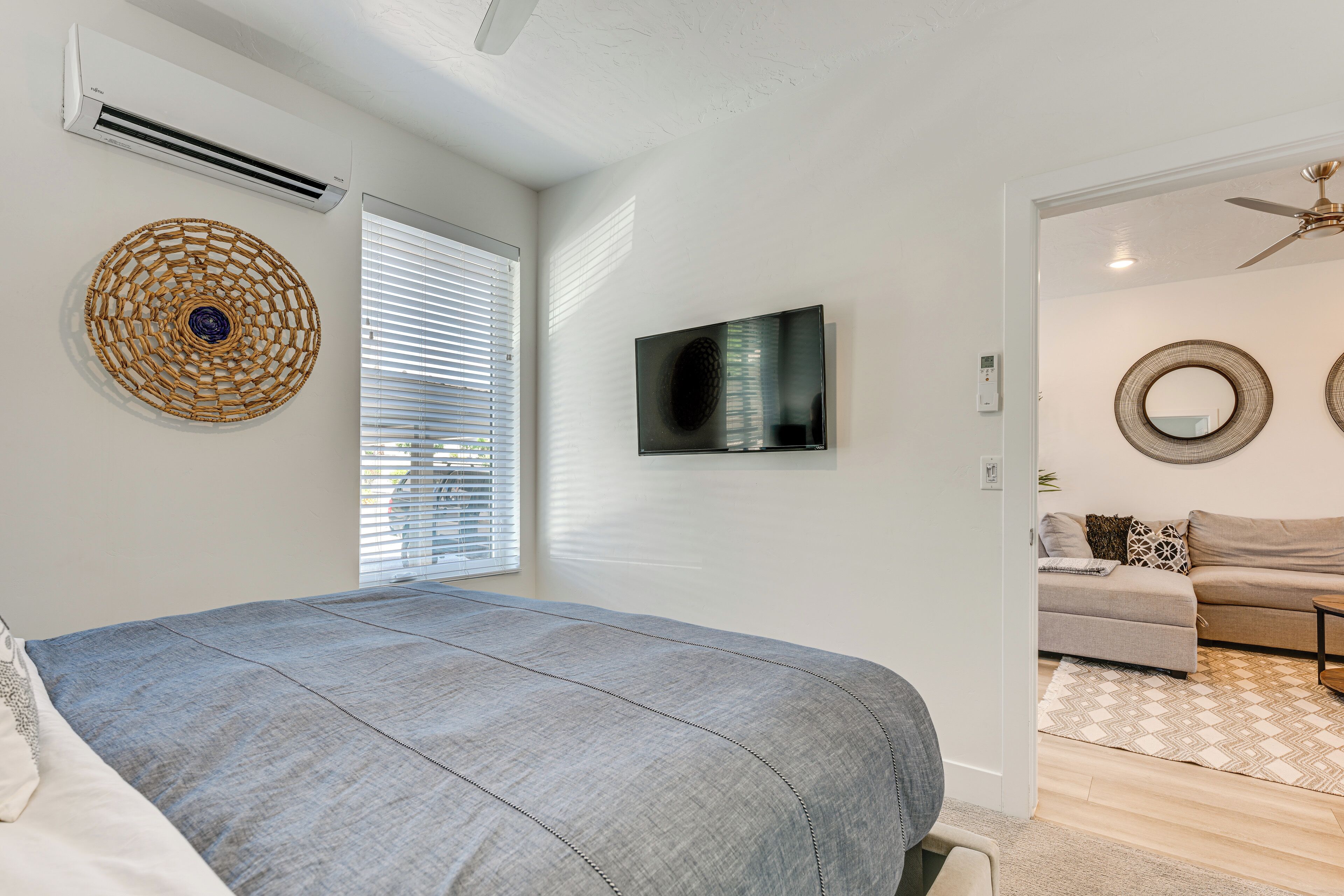 Une chambre dotée d’un lit, d’un appareil de climatisation, d’une télévision et offrant une vue sur le salon, qui comprend un canapé et un ventilateur de plafond.