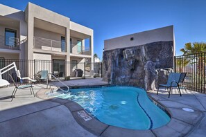 Una piscina con pared de roca, sillas de descanso y un edificio con balcones.