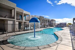 Zona de piscina con fuente de agua, sillas de descanso y fachada de edificio moderna.