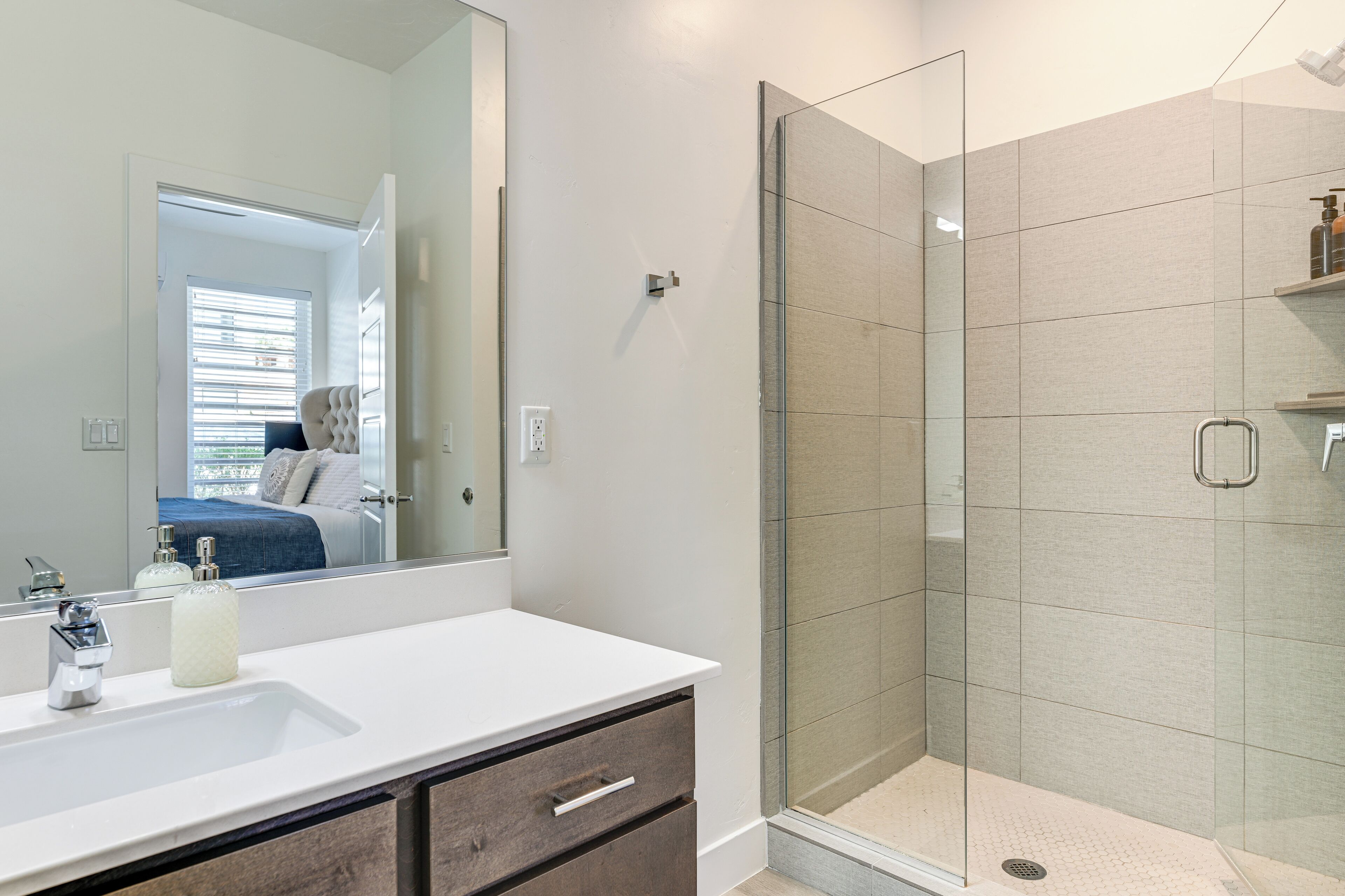 A modern bathroom with a glass-enclosed shower, a white sink, and a large mirror.