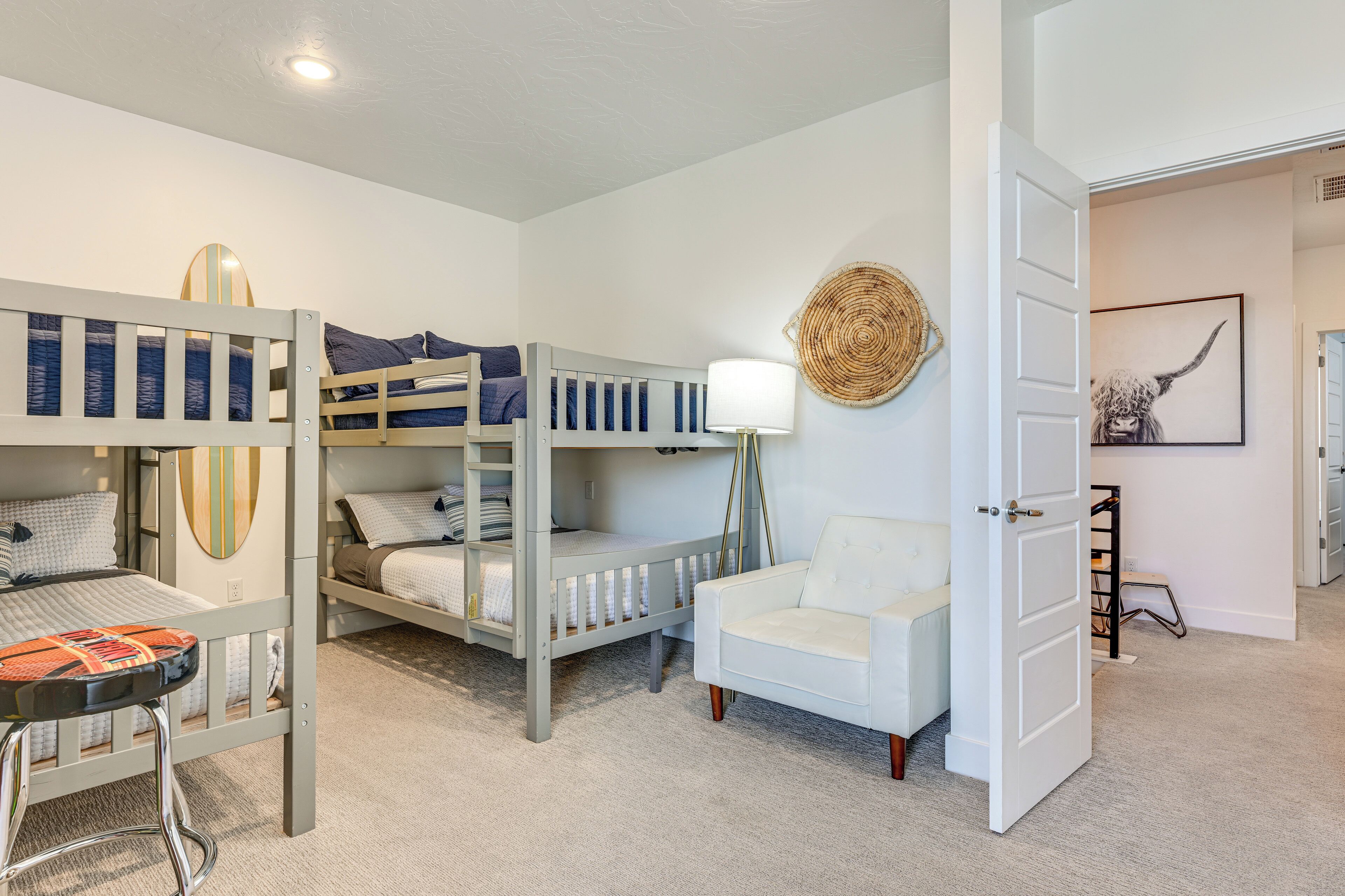 Habitación infantil con literas, una silla blanca y una puerta que da a otra habitación.
