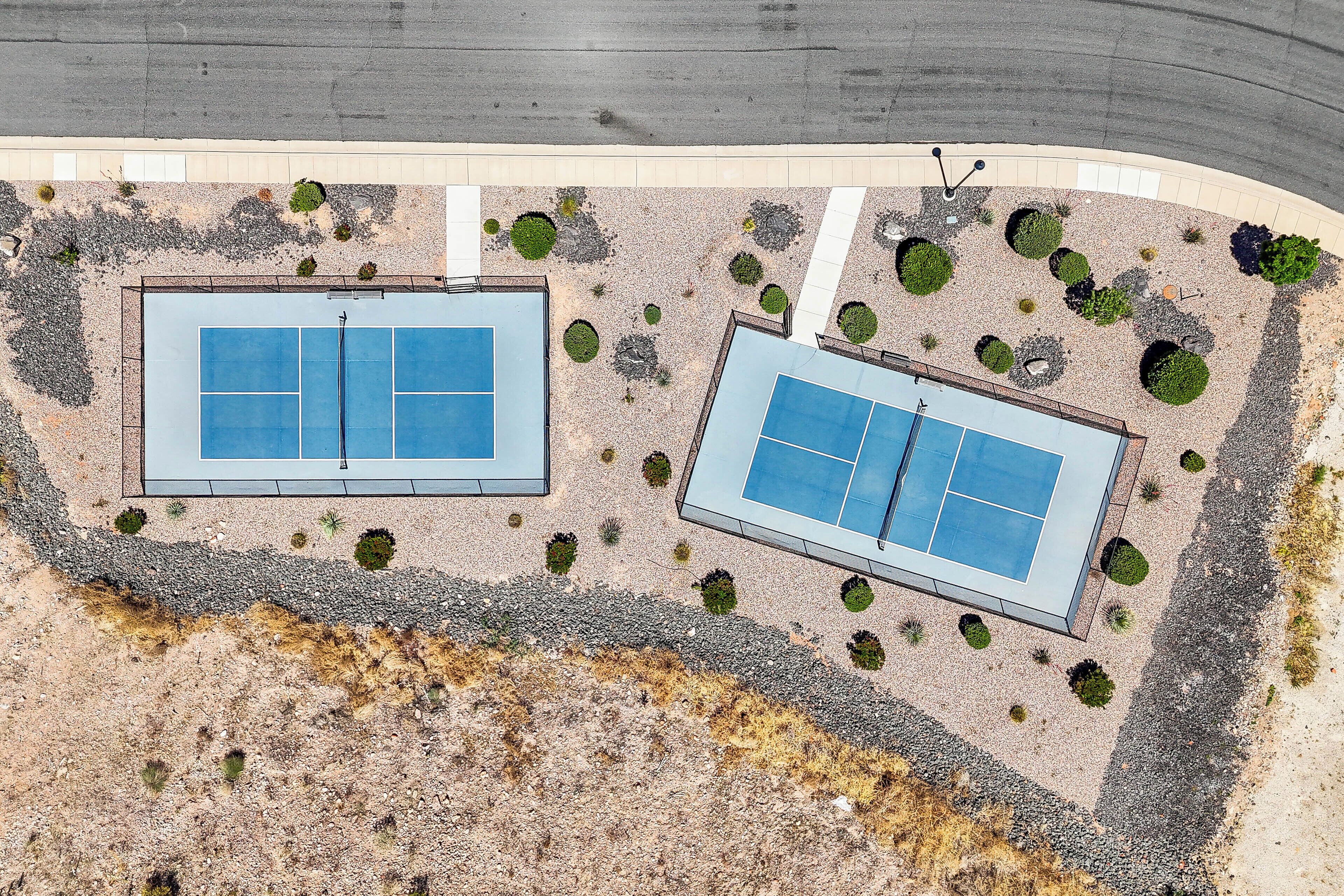 An aerial view of a modern building with two tennis courts surrounded by landscaped areas and a parking lot.