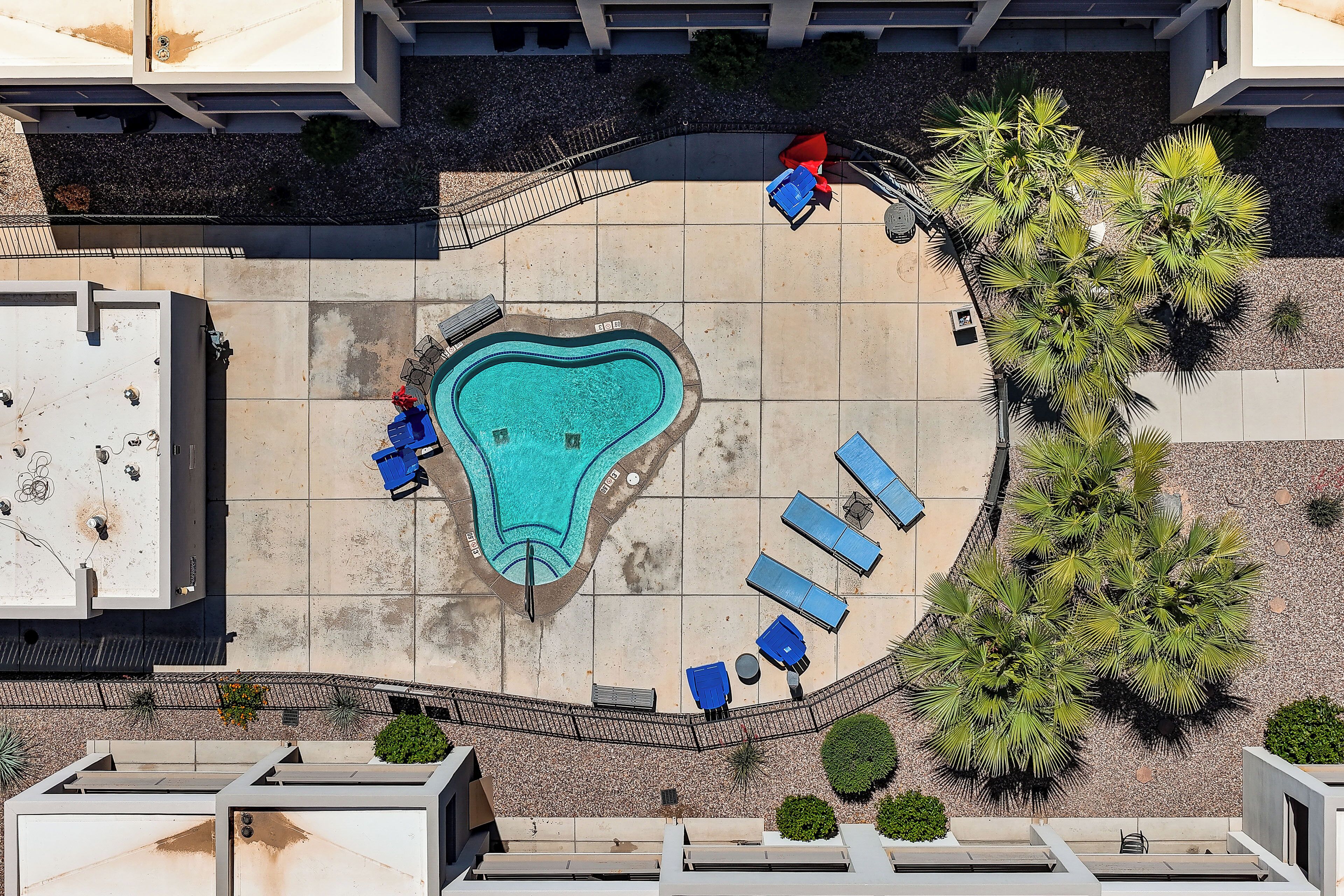 An aerial view of a hotel courtyard with a swimming pool, lounge chairs, and palm trees.
