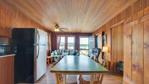 A wooden cabin interior with a dining table, chairs, a refrigerator, a microwave, and a ceiling fan.