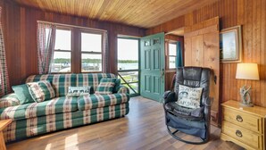 A cozy cabin interior with a plaid sofa, a rocking chair, and a wooden dresser.