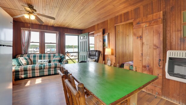 A wooden cabin interior with a green table, plaid sofa, and a ceiling fan. - Beach & Dock Access! Upper Peninsula Cabin Retreat (Cedarville)