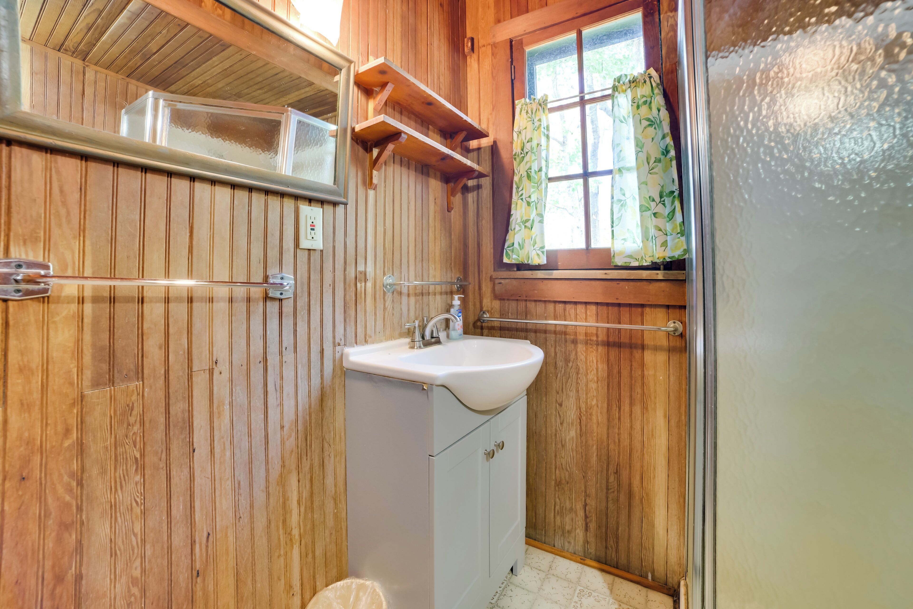 A wooden cabin bathroom with a sink, cabinets, and a window with curtains.