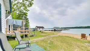 A deck with chairs and a table, a grassy area, and a view of a lake with houses and docks in the background. - Resort Cabin On Lake Huron! Pets Welcome (Cedarville)