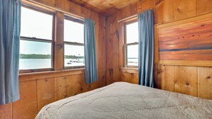 A wooden cabin room with a bed, large windows, and a painting on the wall. - Resort Cabin On Lake Huron! Pets Welcome (Cedarville)