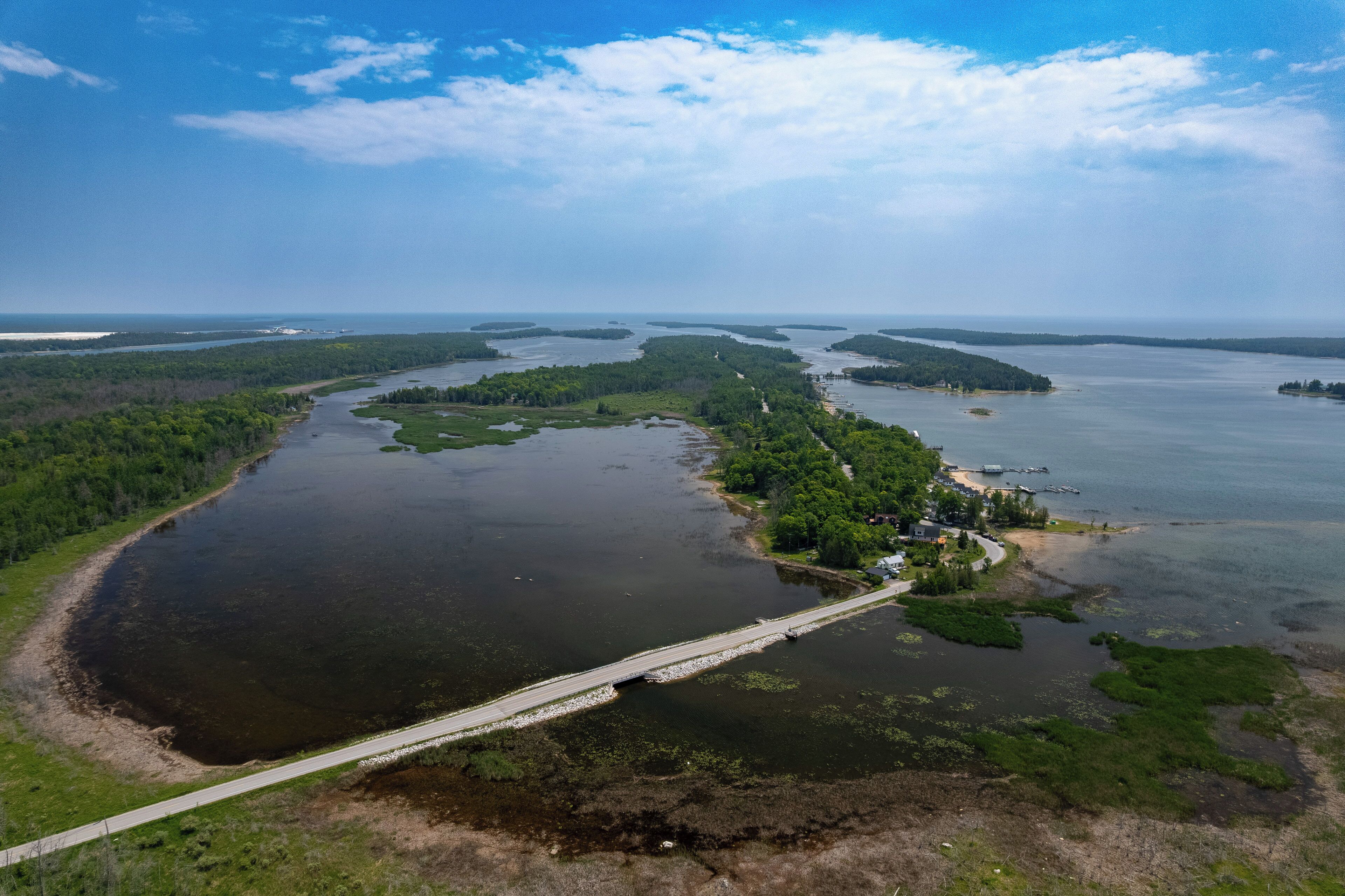 An aerial view of a coastal area with a bridge connecting two landmasses, surrounded by water and greenery.